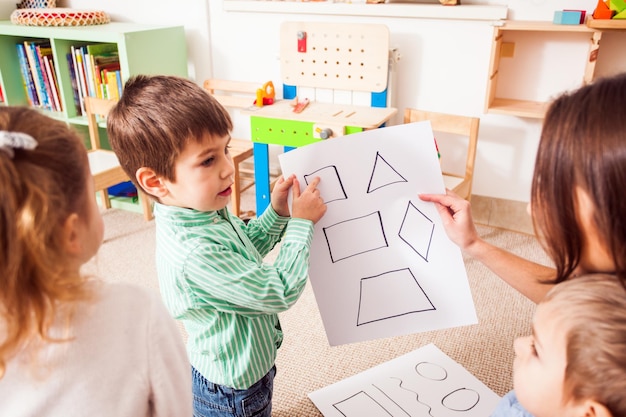 Schöne junge Lehrerin, die Figuren im Vorschulalter zeigt und erklärt, Kinder sitzen im Kreis