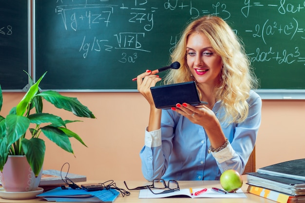 Schöne junge Lehrerin schminkt sich zwischen den Klassen