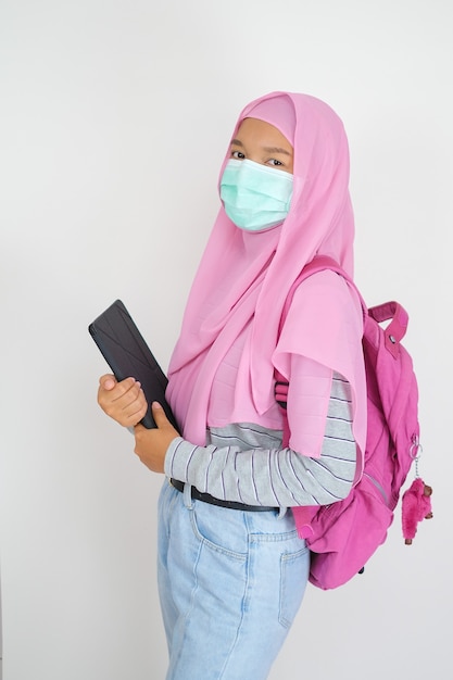 Schöne junge Mädchen tragen rosa Hijab und Maske halten Laptop auf weißem Hintergrund white