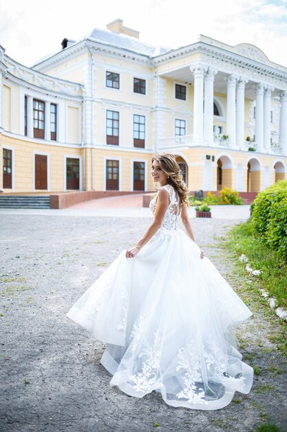 Schöne junge Mädchenbraut in einem weißen Hochzeitskleid mit einem Zug geht in den Park