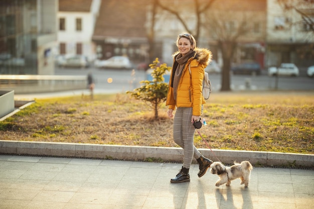 Schöne junge Modefrau verbringt Zeit mit ihrem süßen Hund und geht die Stadtstraße entlang.