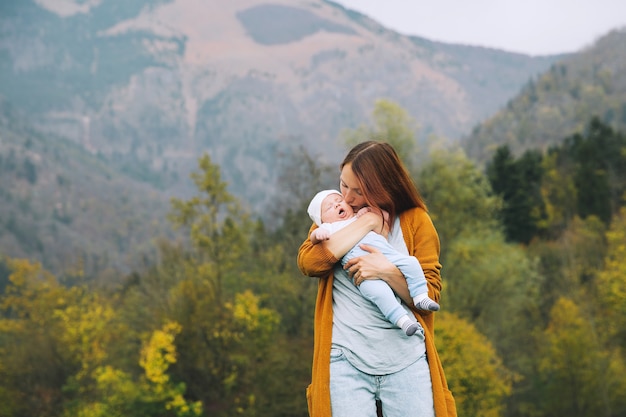 Schöne junge Mutter, die ihr Baby auf dem Hintergrund der Berge in den Armen hält
