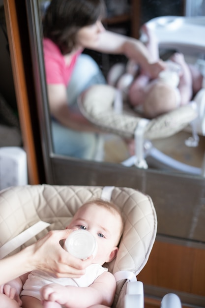 Foto schöne junge mutter, die ihr baby von der flasche einzieht