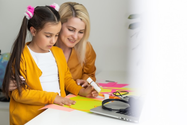 Schöne junge Mutter hilft ihrer jüngeren Tochter bei den Hausaufgaben.