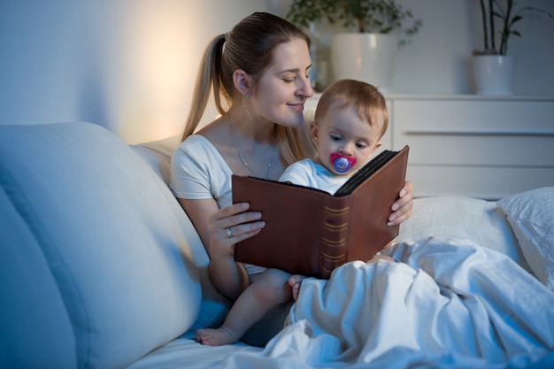 Schöne junge Mutter liest ihrem Baby ein Buch vor dem Einschlafen