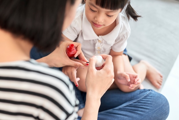 Schöne junge Mutter malt den Nagellack zu ihrer süßen kleinen Tochter