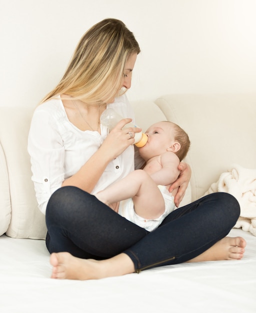 Schöne junge Mutter posiert mit ihrem 6 Monate alten Baby auf dem Bett