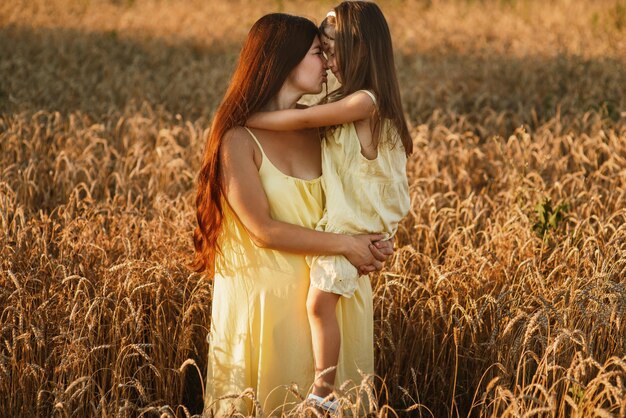 Schöne junge Mutter und ihre kleine Tochter kuscheln und faulenzen bei Sonnenuntergang in einem Weizenfeld