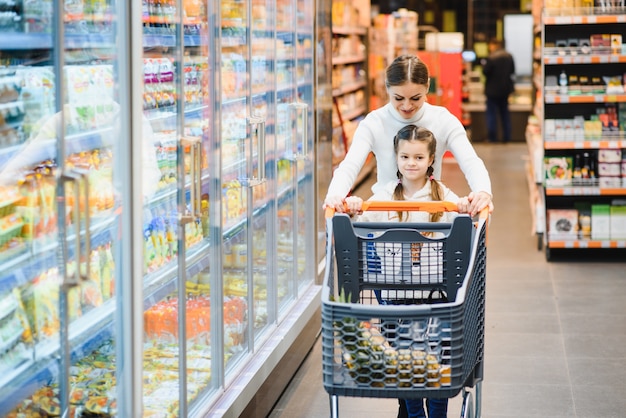 Schöne junge Mutter und ihre kleine Tochter lächeln und kaufen Essen