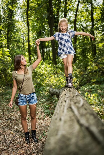 Schöne junge Mutter und ihre Tochter haben Spaß im Wald. Mutter, die ein Mädchen hält, das über einen umgestürzten Baum geht.