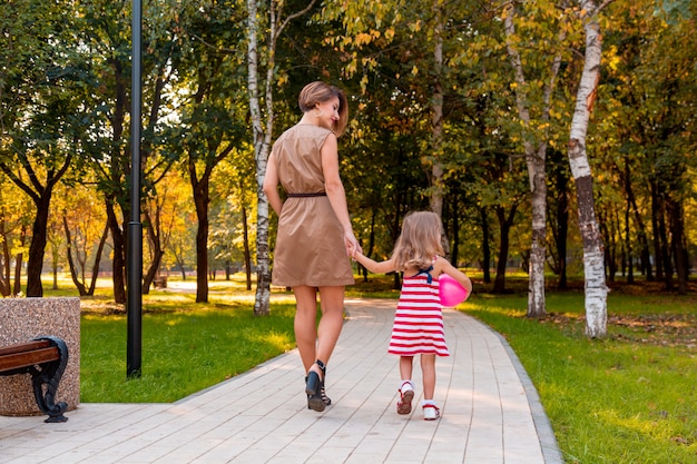 Schöne junge Mutter und Tochter in warmen sonnigen Sommertag. Glückliche Familie Mutter und Kind kleine Tochter spielen und spazieren im Park und genießen die schöne Natur.