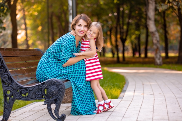 Schöne junge Mutter und Tochter in warmen sonnigen Sommertag. Glückliche Familie Mutter und Kind kleine Tochter spielen und spazieren im Park und genießen die schöne Natur.