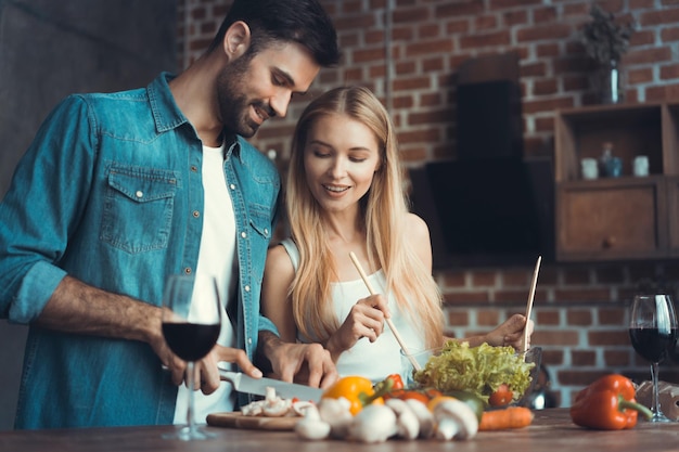 Schöne junge Paare, die zusammen eine gesunde Mahlzeit zubereiten, während sie ihre Freizeit zu Hause verbringen