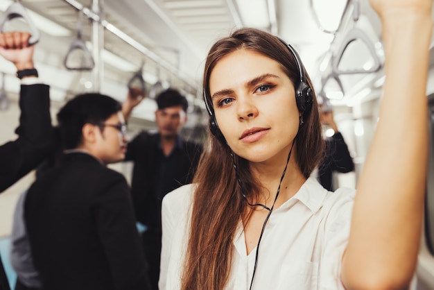 Schöne junge Passagierin, die mit Kopfhörern und während Hemd in der modernen U-Bahn steht