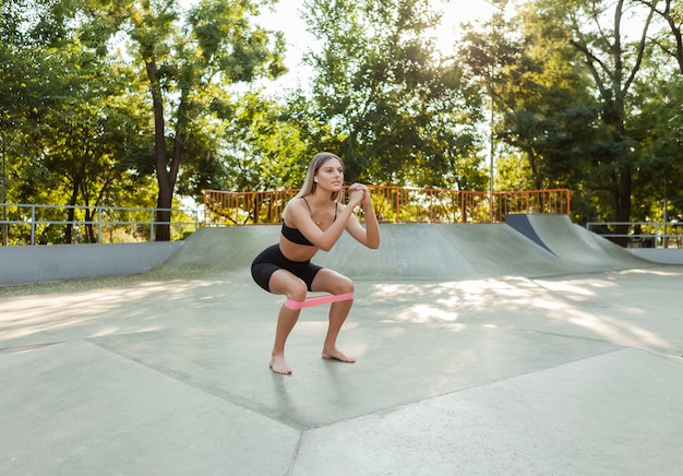 Schöne junge passende Frau macht Morgengymnastik mit Fitness-Gummibändern im Freien.