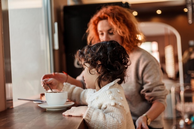 Schöne junge rothaarige Mutter mit süßer lockiger Tochter sitzt in einem gemütlichen Café und trinkt heiße Schule Mothers Day Warm