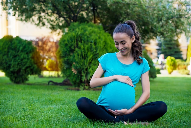 Schöne junge ruhige schwangere Frau sitzt in der Lotussitz und meditiert, während sie Yoga im Park praktiziert