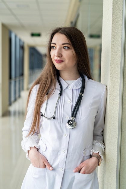 Schöne junge Ärztin steht mit einem Stethoskop um den Hals im Krankenhauskorridor