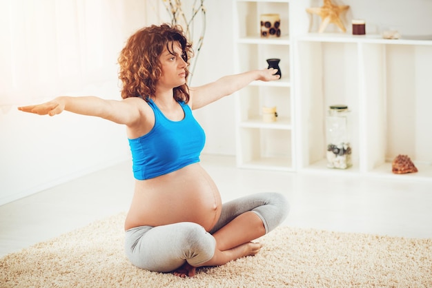 Schöne junge schwangere Frau, die zu Hause Übungen macht.