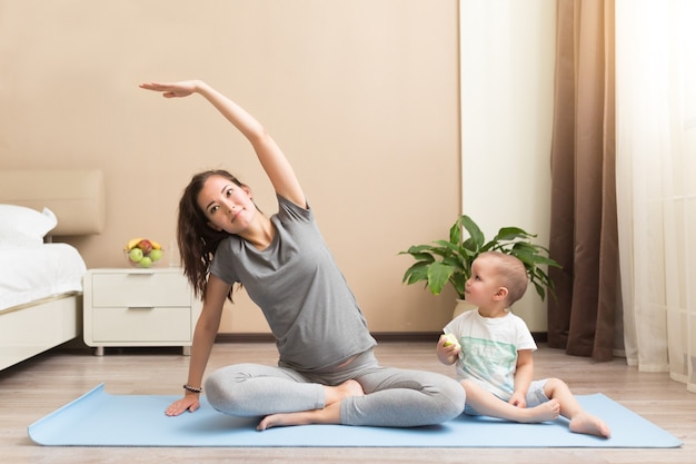 Schöne junge schwangere Frau und kleiner Junge lächelnd beim Liegen auf Yogamatte