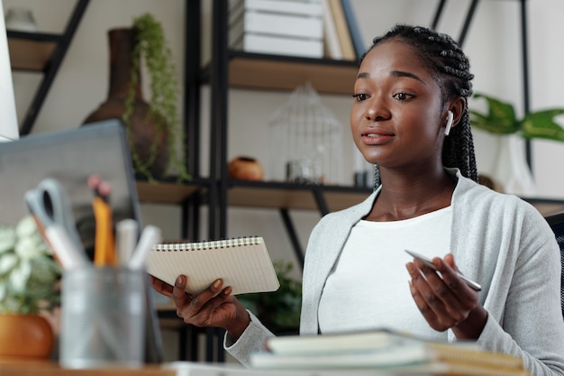 Schöne junge schwarze Frau mit Notebook in der Hand, die ein Online-Meeting mit Kunden oder Mitarbeitern hat und das Projekt bespricht