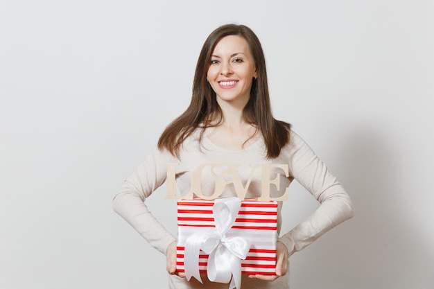 Schöne junge sexy lächelnde Frau, die roten Präsentkarton mit Geschenk, hölzerne Wortliebe auf weißem Hintergrund hält. Kopieren Sie Platz für Werbung. Valentinstag- oder Internationaler Frauentag-Konzept.