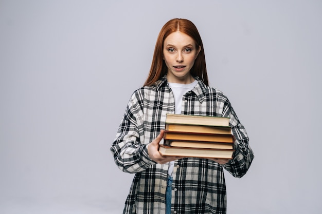 Schöne junge Studentin hält Bücher aus und schaut auf isoliertem Hintergrund in die Kamera