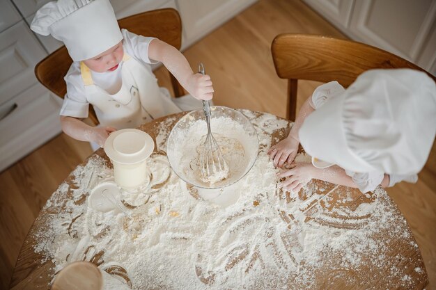 Schöne Junge und Mädchen in Köchenhüten und Schürzen spielen mit dem Mehl in der Küche