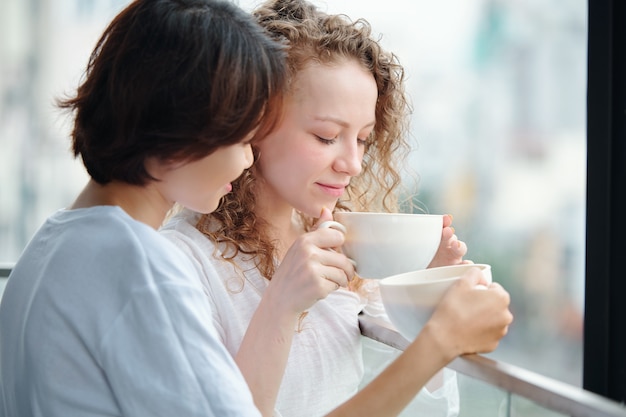 Schöne junge verliebte Frauen trinken Morgenkaffee auf Balkon