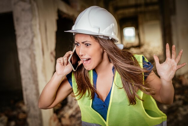 Schöne junge weibliche Bauarchitekten, die auf einer Baustelle telefonieren.