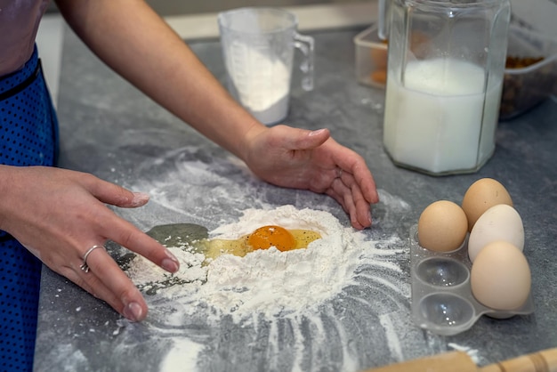 Schöne junge weibliche Hände brechen Eier in Mehl, um einen schönen Teig zu kneten