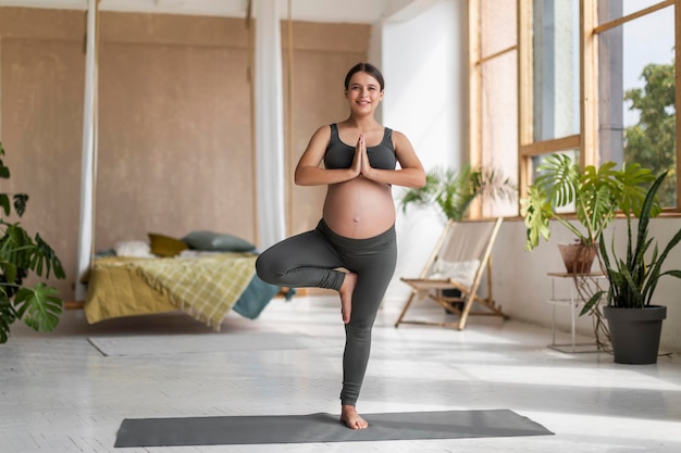 Schöne junge werdende Dame, die zu Hause Yoga in Baumhaltung praktiziert