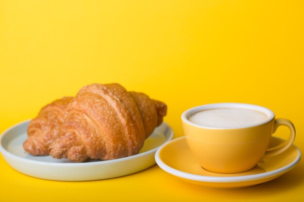 Schöne kaffeegelbe Tasse Cappuccino mit Croissant auf gelbem Hintergrund