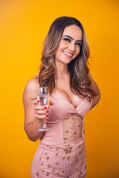 Schöne kaukasische Frau auf gelbem Hintergrund, die ein Glas Champagner hält und feiert.