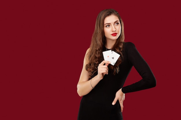 Schöne kaukasische Frau im schwarzen Kleid mit Pokerkarten, die im Casino spielen