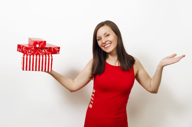 Schöne kaukasische junge glückliche Frau kleidete im roten Kleid an und verbreitete Hände des Weihnachtshutes, die Geschenkboxen auf weißem Hintergrund halten. Sankt-Mädchen mit dem Geschenk lokalisiert. Neujahrsfeiertag 2018 Konzept.