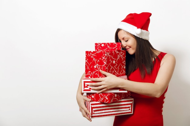 Schöne kaukasische junge glückliche Frau mit charmantem Lächeln, gekleidet in rotem Kleid und Weihnachtsmütze mit Geschenkboxen auf weißem Hintergrund. Sankt-Mädchen mit dem Geschenk lokalisiert. Neujahrsferien 2018 Konzept