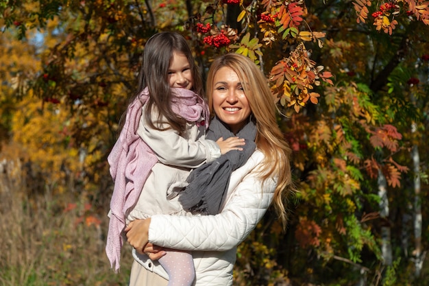 Schöne kaukasische Mutter umarmt Tochter auf Hintergrund der sonnigen Herbstbäume. Konzept Familienwochenende, Liebe, Entspannung im Freien, Spaß, Menschen, Jahreszeit, warmes Wetter, malerische Wälder