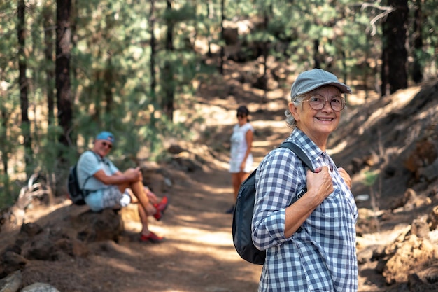 Schöne kaukasische Seniorin mit Hut und Rucksack, die mit Freunden auf einer Bergwanderung spazieren geht und Freizeit und Freiheit in der Natur genießt Senioren im Ruhestand und gesundes Lebensstilkonzept