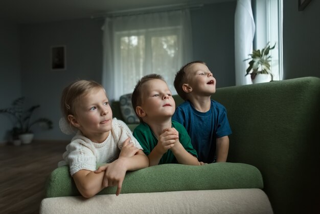 Schöne kinder, die zu hause auf dem sofa liegen, schauen neugierig aus dem fenster. .