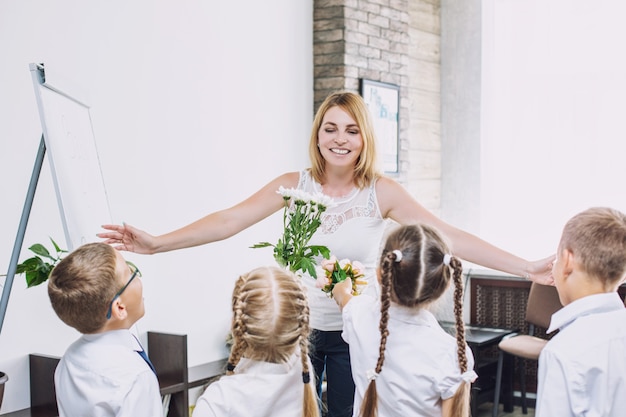 Schöne Kinderschulkinder mit Blumen für die Lehrer in der Schule an einem Feiertag