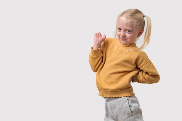 Schöne kleine blonde Mädchen in gelbem Pullover und grauen Hosen posieren auf weißem Hintergrund