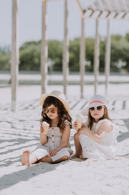 Schöne kleine Mädchen in weißem Kleid und Hut, die im Sommer Eis am Strand essen