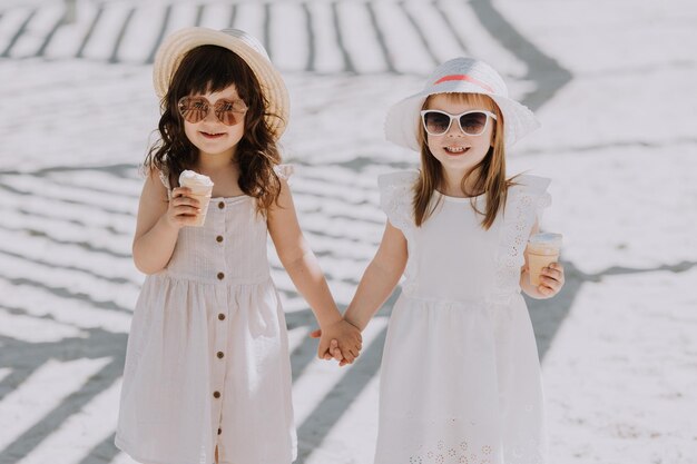 Schöne kleine Mädchen in weißem Kleid und Hut, die im Sommer Eis am Strand essen