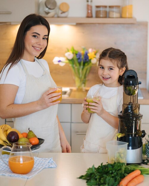 Schöne kleine Mädchen trinken frischen Saft mit ihrer Mutter zu Hause zwei Weibchen in Schürze Früchte und