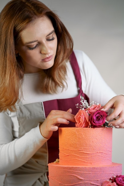Schöne Konditorin in einer Arbeitsschürze schmückt einen Geburtstagskuchen mit frischen Blumen