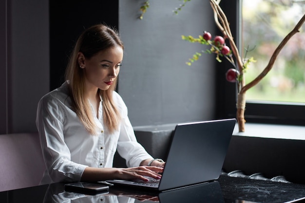 Schöne konzentrierte bei der Arbeit junge freiberufliche Frau, die am Arbeitsplatz sitzt und am Laptop arbeitet.