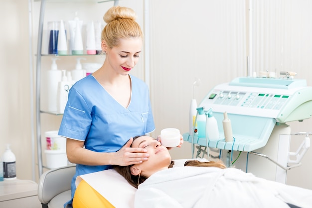 Schöne Kosmetikerin in Uniform, die dem Patienten im Kosmetikbüro eine Gesichtsbehandlung macht