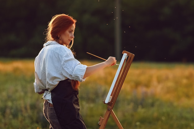 Schöne Künstlerin, die bei Sonnenuntergang in der Natur malt