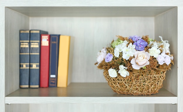 Schöne künstliche Blume im Korb auf dem Bücherregal in der Bibliothek